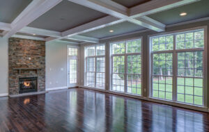 The interior home design of a family room with high ceilings, a fireplace, and a wall of windows designed by CarrHomes in Hamilton.